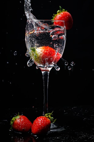A vibrant image showing a glass of water with a strawberry pastille dissolving, next to fresh strawberries and an orange pastille with slices of orange.