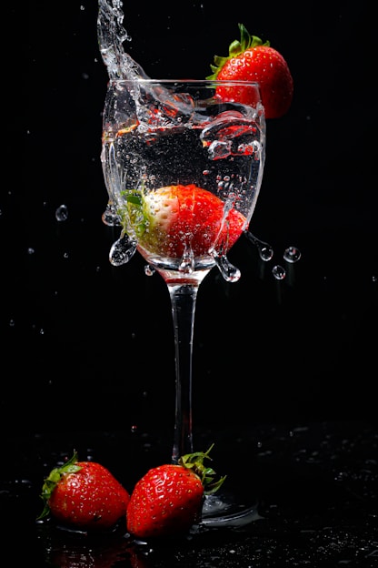 A vibrant image showing a glass of water with a strawberry pastille dissolving, next to fresh strawberries and an orange pastille with slices of orange.