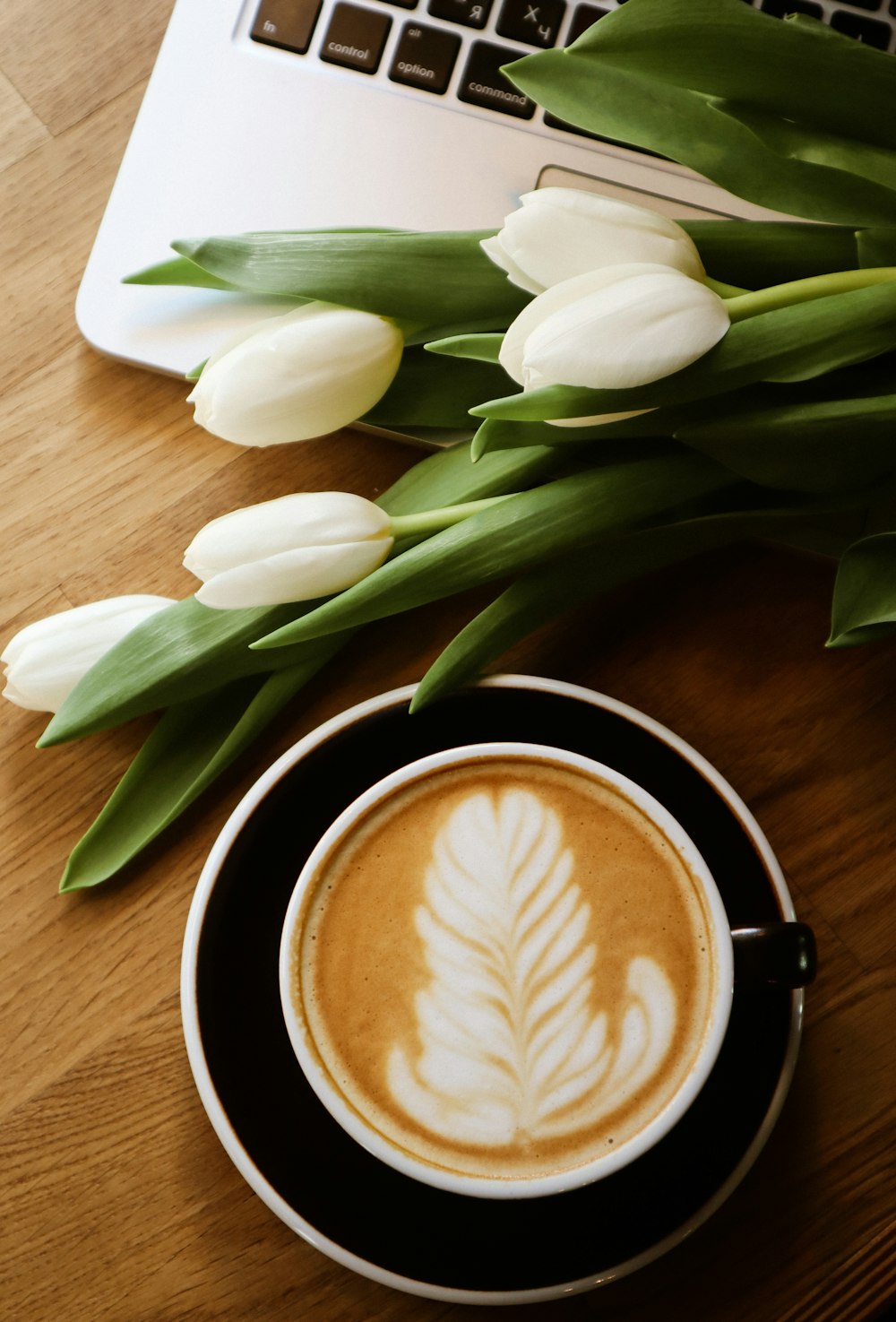 white tulips beside brown and white ceramic mug with coffee
