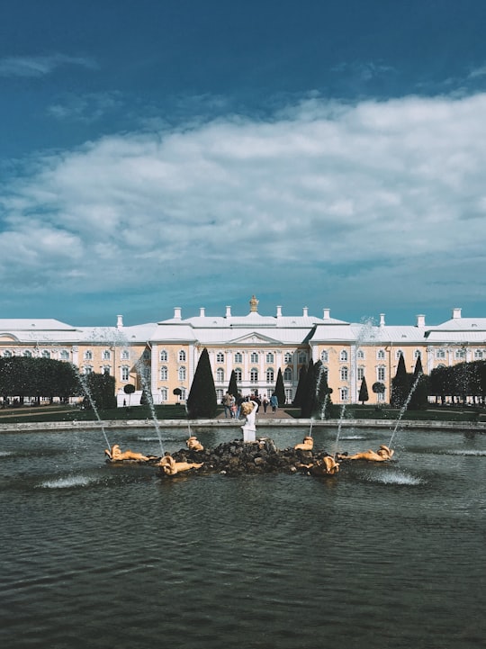 people riding on boat on water near white concrete building during daytime in Grand Peterhof Palace Russia