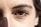 A close-up view of a person's eye with detailed focus on the eyelashes and eyebrow. The lighting highlights the texture of the skin around the eye, casting a subtle shadow.
