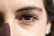 A close-up view of a person's eye with detailed focus on the eyelashes and eyebrow. The lighting highlights the texture of the skin around the eye, casting a subtle shadow.