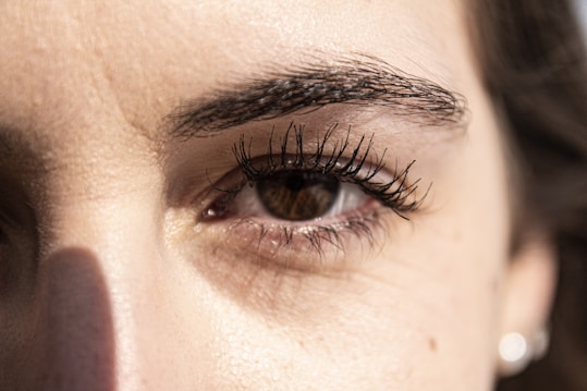 A close-up view of a person's eye with detailed focus on the eyelashes and eyebrow. The lighting highlights the texture of the skin around the eye, casting a subtle shadow.