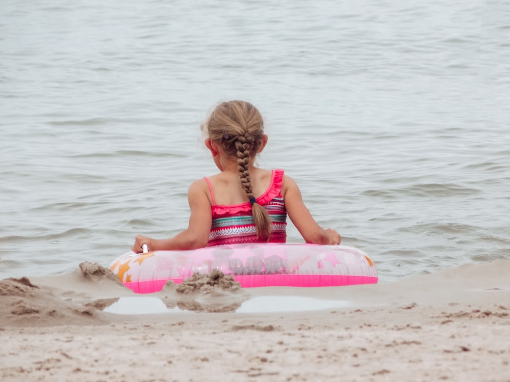 girl in red and white stripe tank top sitting on pink surfboard on beach during daytime