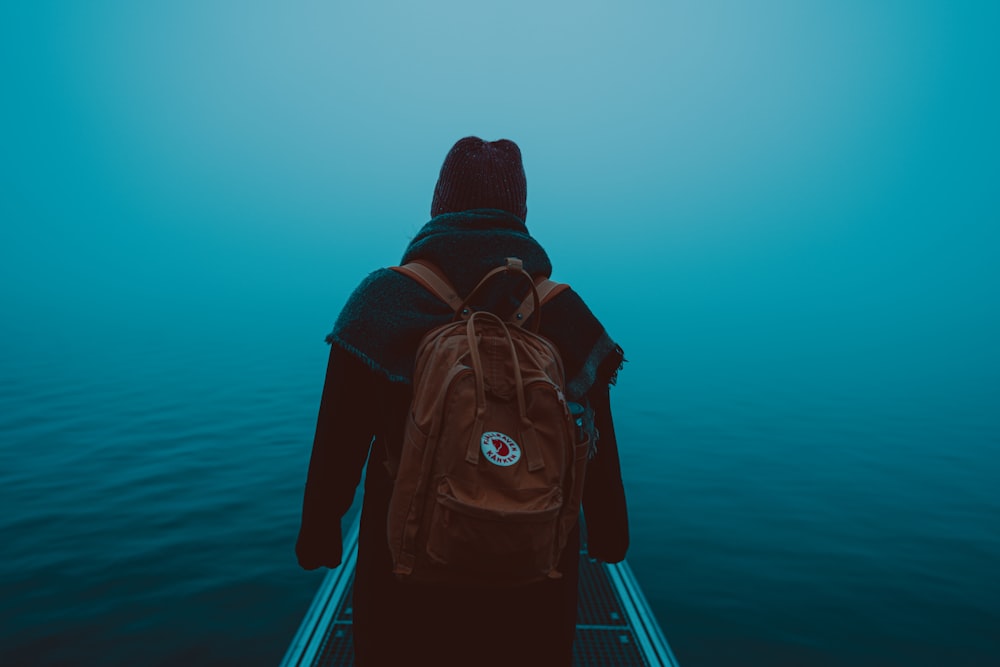 person in black and red hoodie wearing black backpack standing on dock during daytime