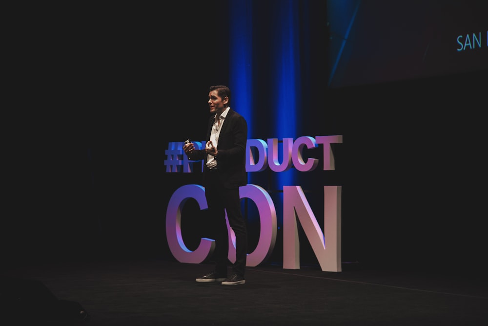 man in black suit standing on stage