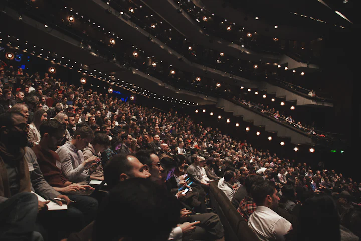 A large audience seated in rows in a darkened hall.