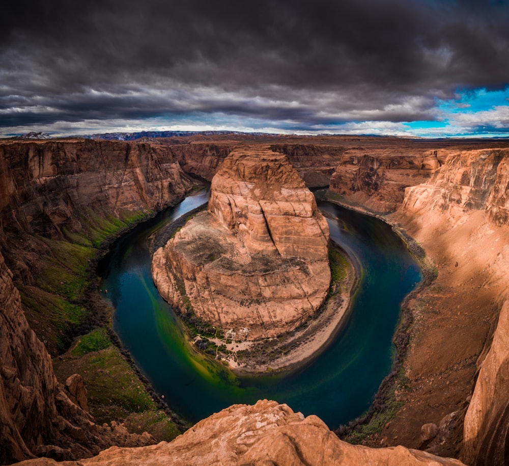 Braune Felsformation in der Nähe von blauem Wasser unter grauen Wolken