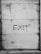 A corrugated metal shutter with the word 'EXIT' spray-painted in black. The shutter appears weathered and aged, with visible signs of rust and dirt. It is closed and secured at the bottom.