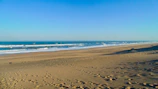 Sandy beach with footprints leading towards the gentle waves under a clear blue sky.