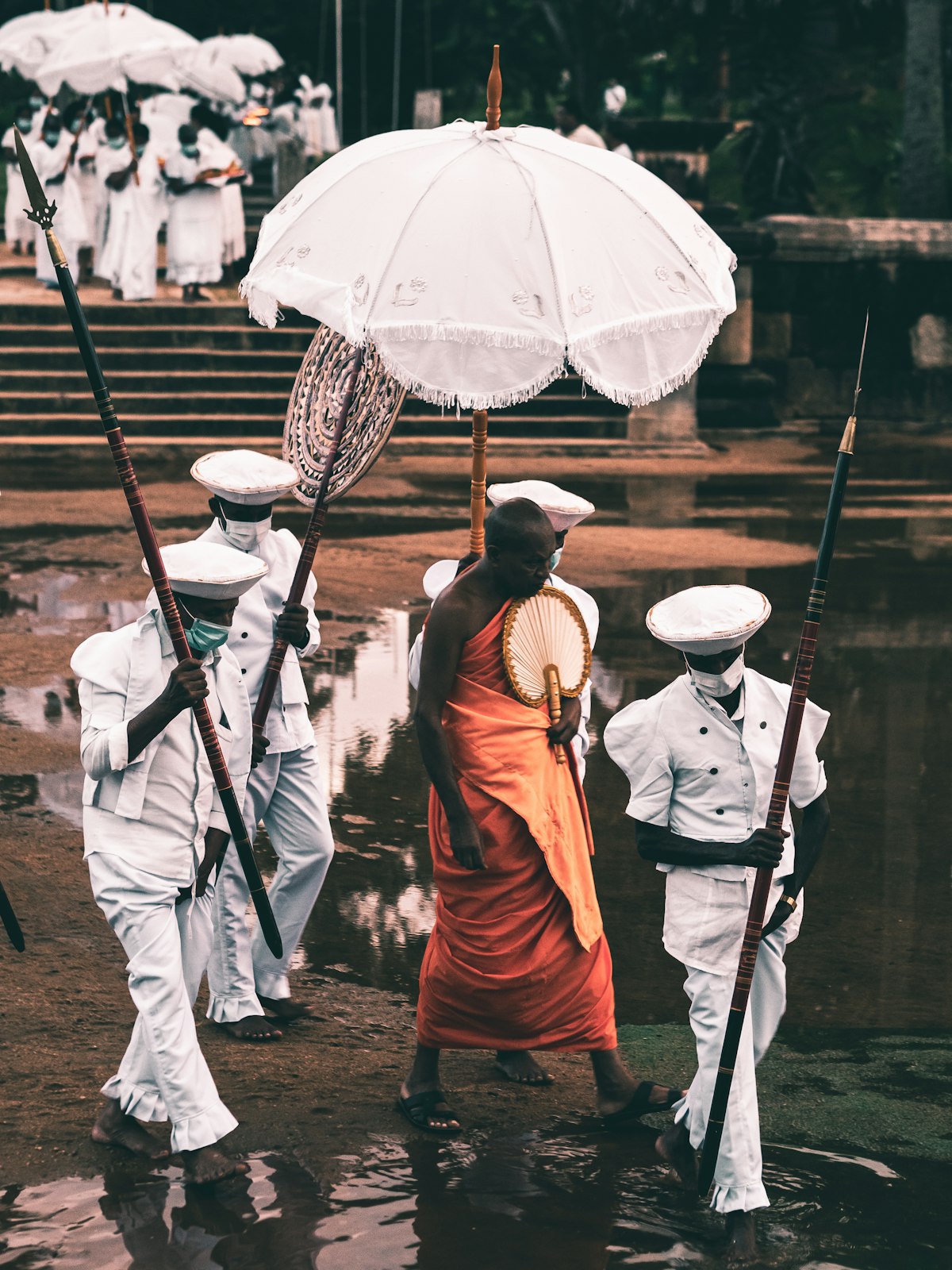 Pilgrims in orange robes walking with umbrellas on a rain-soaked path