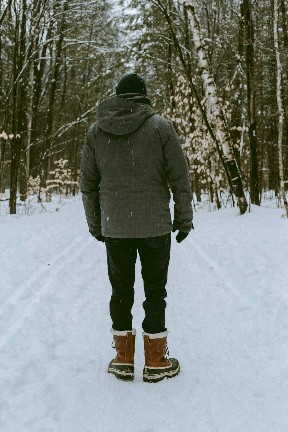 person in gray jacket and black pants standing on snow covered ground during daytime