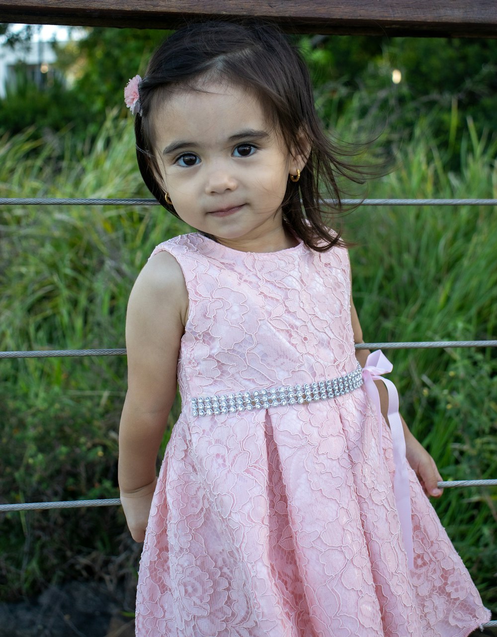 girl in pink sleeveless dress standing near gray metal fence during daytime