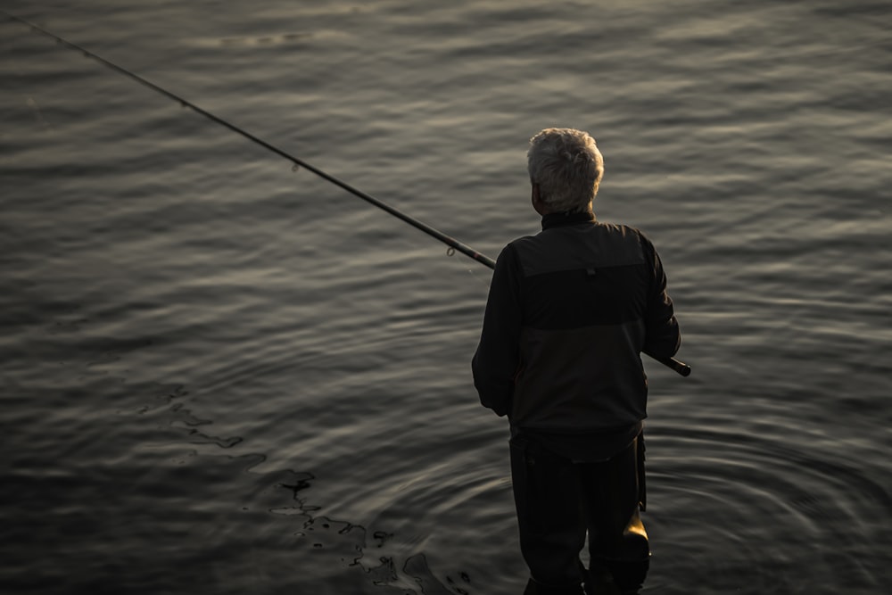 man in black jacket and black pants holding black fishing rod