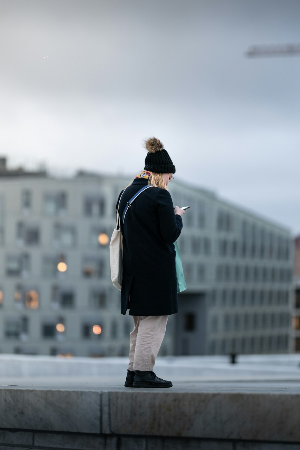 donna in cappotto nero e pantaloni grigi in piedi sul pavimento di cemento grigio durante il giorno