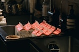 Several milk cartons with open tops are placed in an industrial-style metal sink, surrounded by various kitchen items including bottles and containers. The cartons have red and white labels with text in a foreign language.