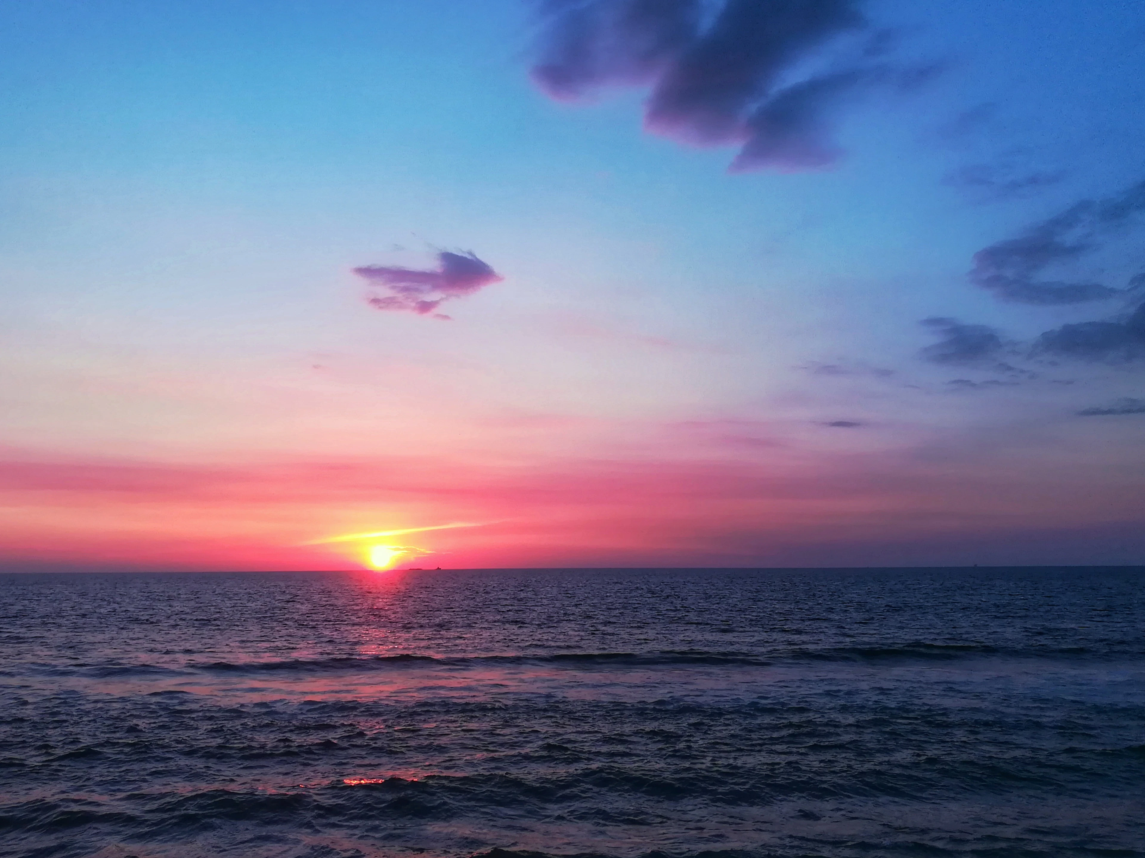 Vivid pink and purple sunset colors over a calm ocean horizon with gentle waves.