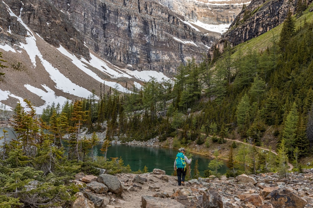 man in blue shirt and blue backpack standing on rock near river during daytime