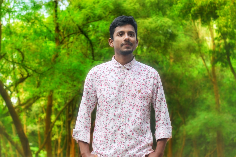man in white and red floral button up t-shirt standing near green trees during daytime