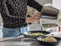 woman in blue denim jeans holding stainless steel cooking pot