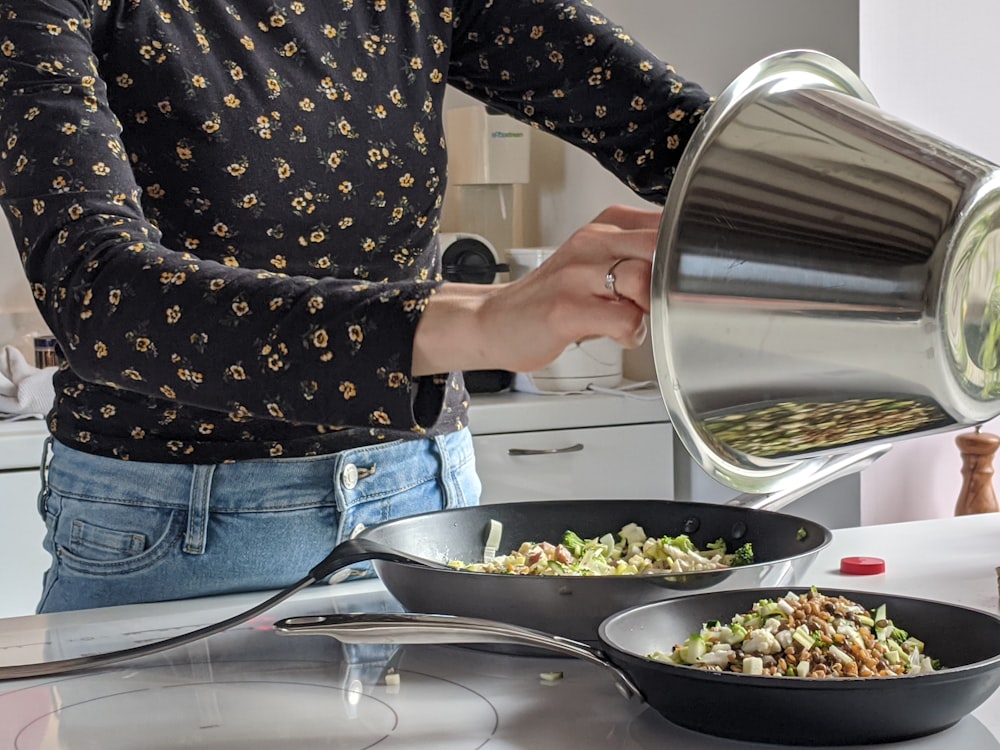 woman in blue denim jeans holding stainless steel cooking pot