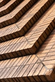 Rows of uniformly stacked reddish-brown bricks arranged in a stepped pattern, creating a geometric and orderly facade. The bricks appear aged with a few containing subtle cracks and discolorations, likely from weather exposure.