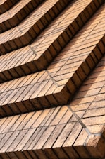 Rows of uniformly stacked reddish-brown bricks arranged in a stepped pattern, creating a geometric and orderly facade. The bricks appear aged with a few containing subtle cracks and discolorations, likely from weather exposure.