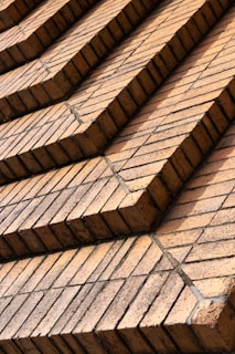 Rows of uniformly stacked reddish-brown bricks arranged in a stepped pattern, creating a geometric and orderly facade. The bricks appear aged with a few containing subtle cracks and discolorations, likely from weather exposure.