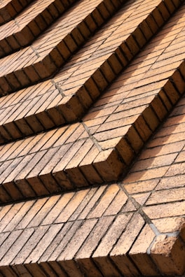 Rows of uniformly stacked reddish-brown bricks arranged in a stepped pattern, creating a geometric and orderly facade. The bricks appear aged with a few containing subtle cracks and discolorations, likely from weather exposure.