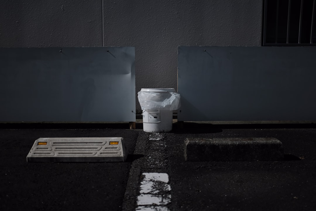 white plastic trash bin beside blue wall