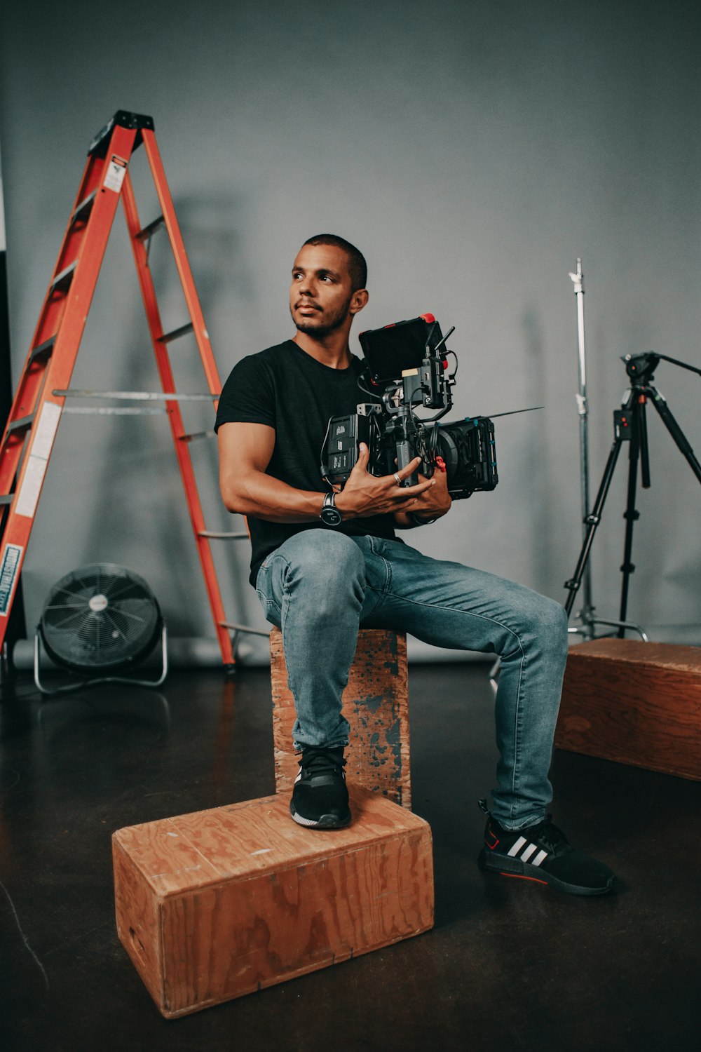 man in black crew neck t-shirt and blue denim jeans sitting on brown wooden stool