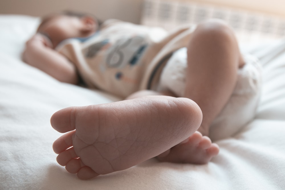 baby in white and green onesie lying on bed