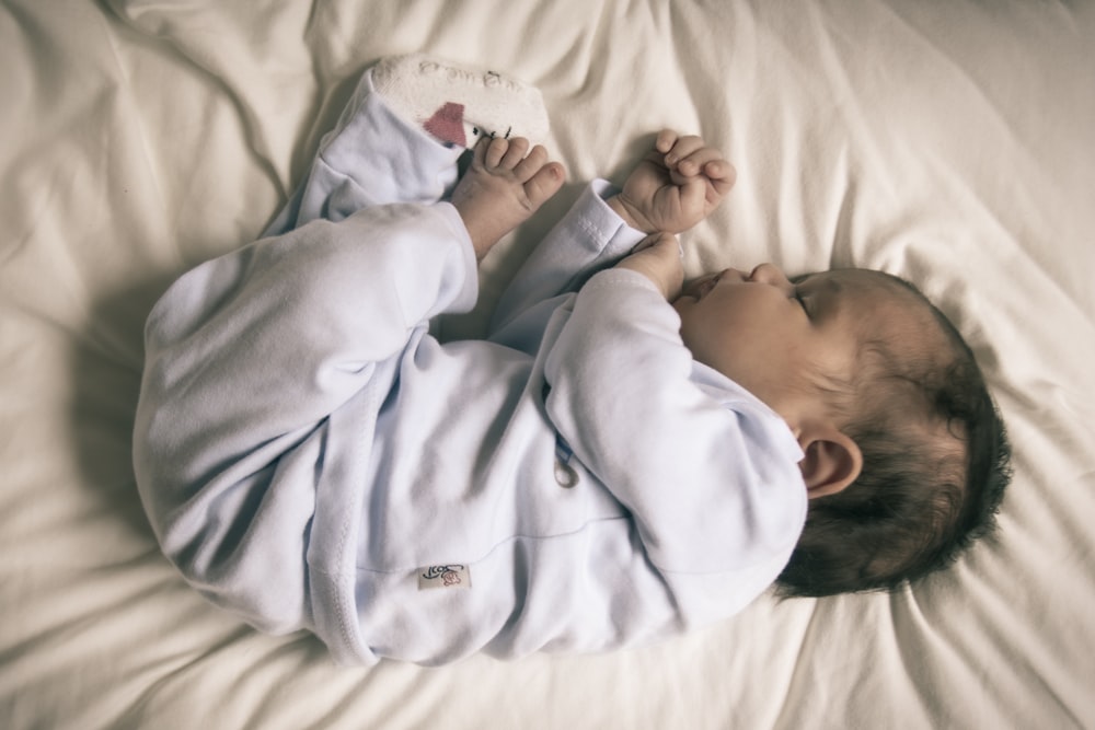 baby in blue blanket sleeper lying on bed