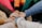 A group of people stand in a circle with their hands stacked on top of each other in the center, suggesting unity and teamwork. They are wearing colorful sweaters.