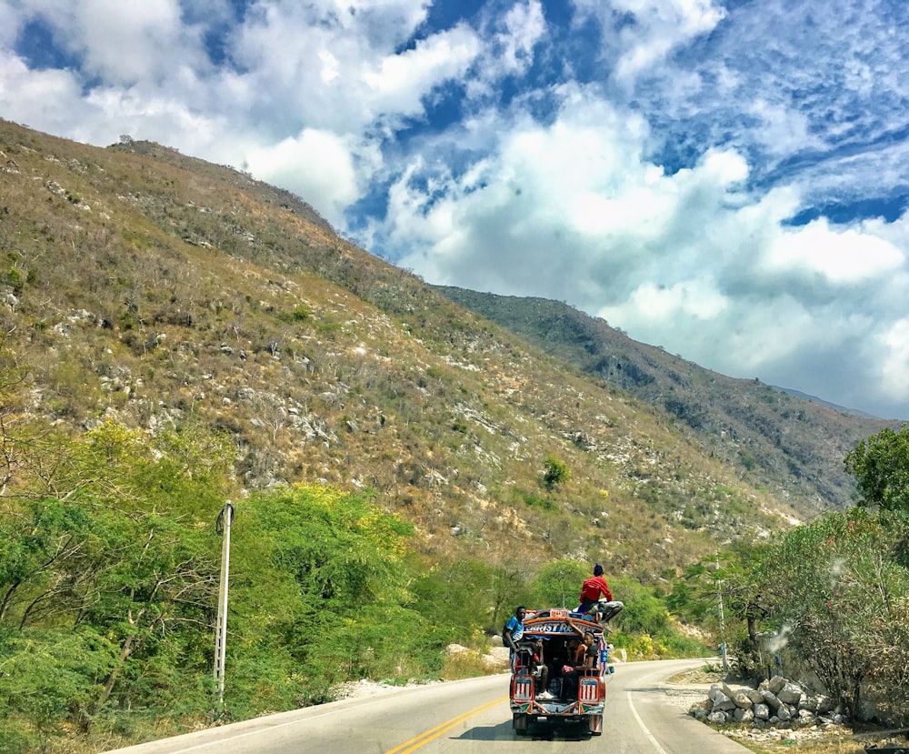 red and black motorcycle on road near green mountain under blue and white cloudy sky during