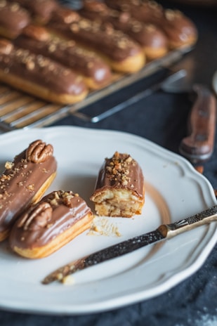 Close-up of a glossy chocolate éclair with delicate gold leaf decoration on a dark plate.