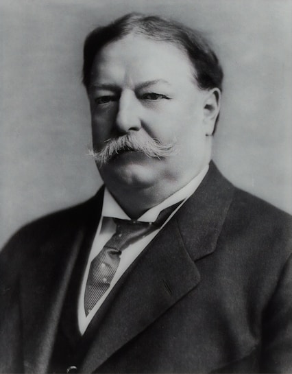 A black and white portrait of a distinguished man with a mustache, wearing a suit and tie. The image has a formal and historical feel.