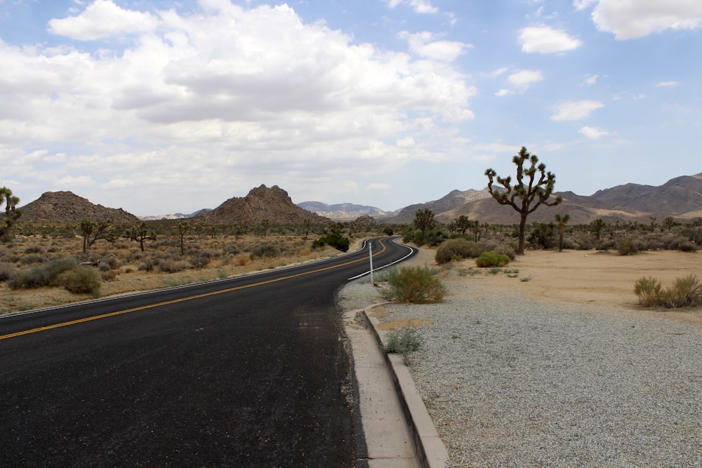 gray concrete road near brown mountain under white clouds during daytime