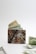 A camouflage-patterned wallet is open, with visible US dollar bills partially sticking out. Additional bills are scattered on the flat surface in front of the wallet, with a plain white background giving a minimal and clean appearance.