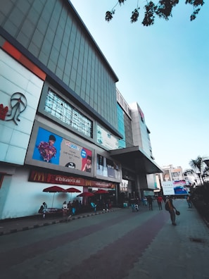 Modern shopping mall exterior near the shore with shoppers walking by on a sunny day.