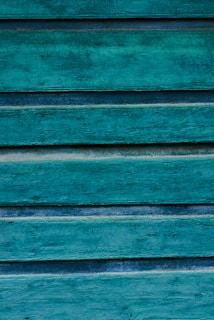 Weathered wooden panels painted in a vibrant teal color, displaying a rustic and textured surface with visible grain patterns and variations in the paint.
