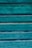 Weathered wooden panels painted in a vibrant teal color, displaying a rustic and textured surface with visible grain patterns and variations in the paint.