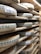 Rows of large, round cheese wheels are stacked on wooden shelves in a storage or aging room. Each cheese wheel is wrapped with a label, indicating that the cheeses are Comté. The shelves are made of unfinished wood, creating a rustic and traditional atmosphere.