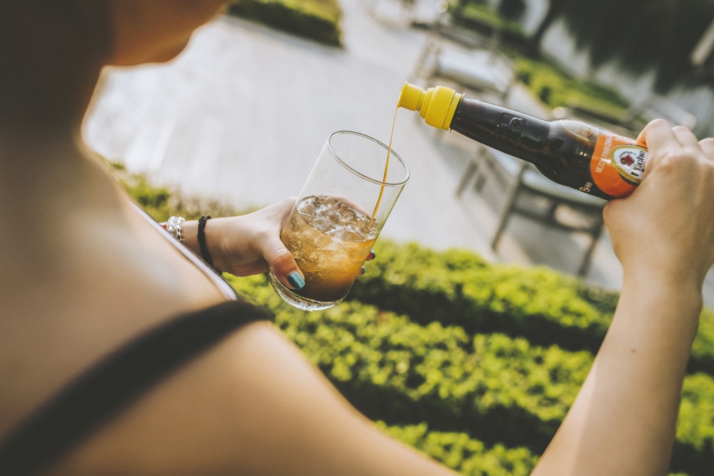 person holding clear drinking glass with brown liquid