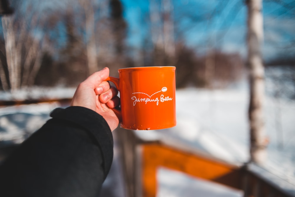 person holding orange ceramic mug