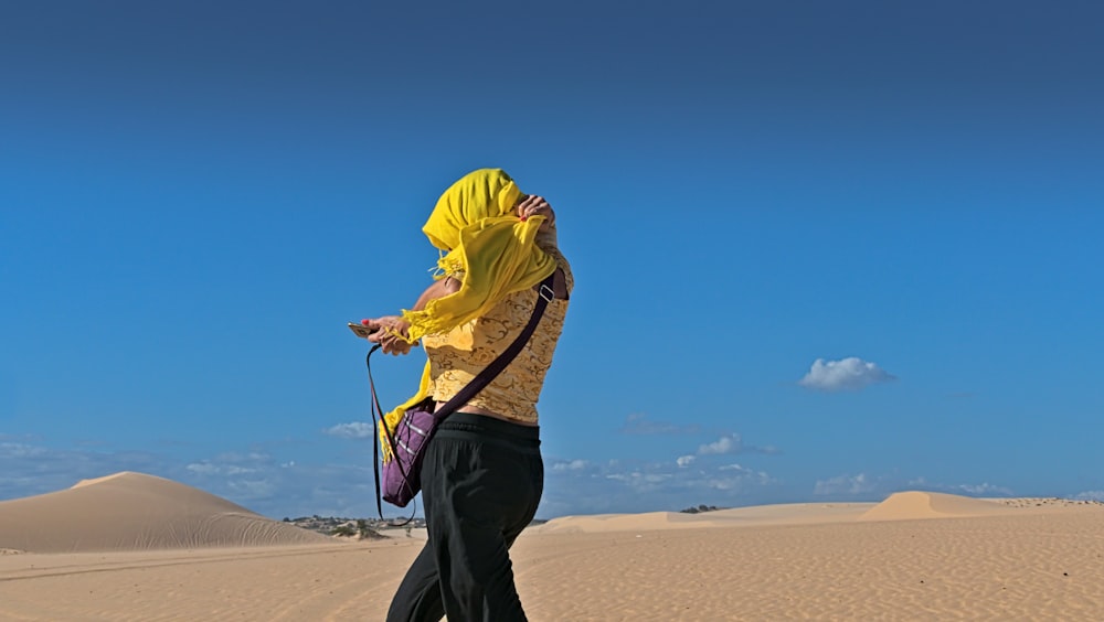 homem em capuz amarelo e calças pretas com saco de estilingue preto andando na areia durante o dia