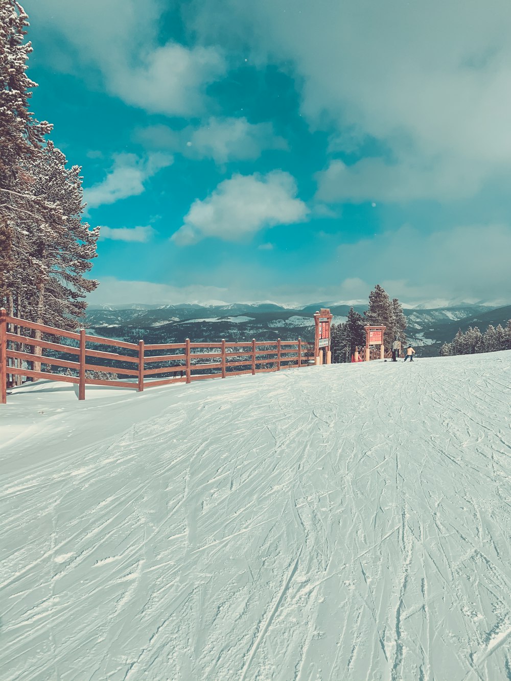 valla de madera marrón en el suelo cubierto de nieve bajo el cielo azul y las nubes blancas durante el día