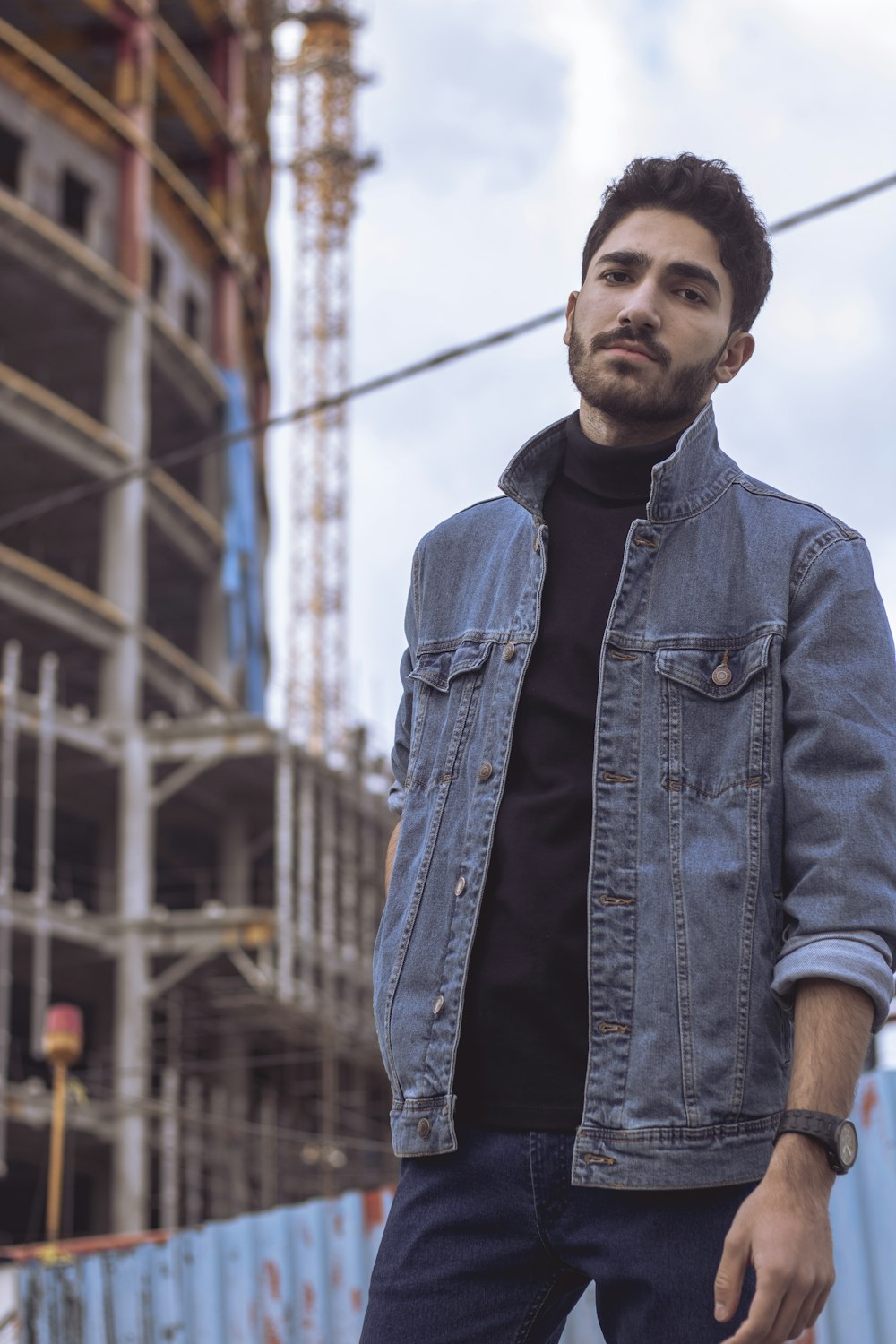 man in blue denim jacket standing near building during daytime