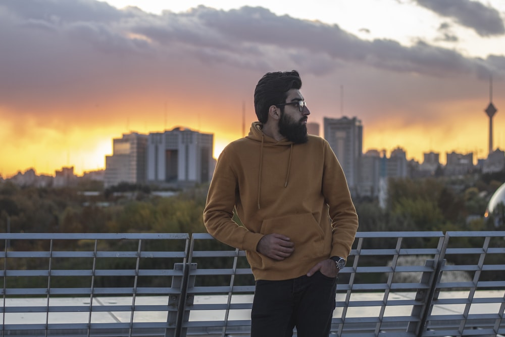 man in brown hoodie standing on bridge during sunset