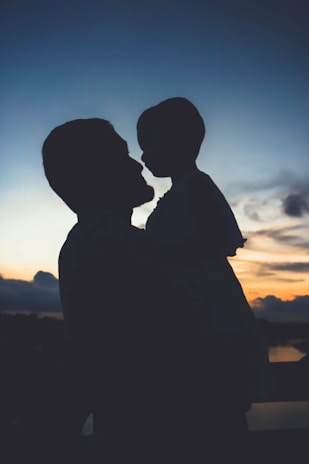 A sunset silhouette of a child carrying a younger sibling on their back, illustrating deep bonds.